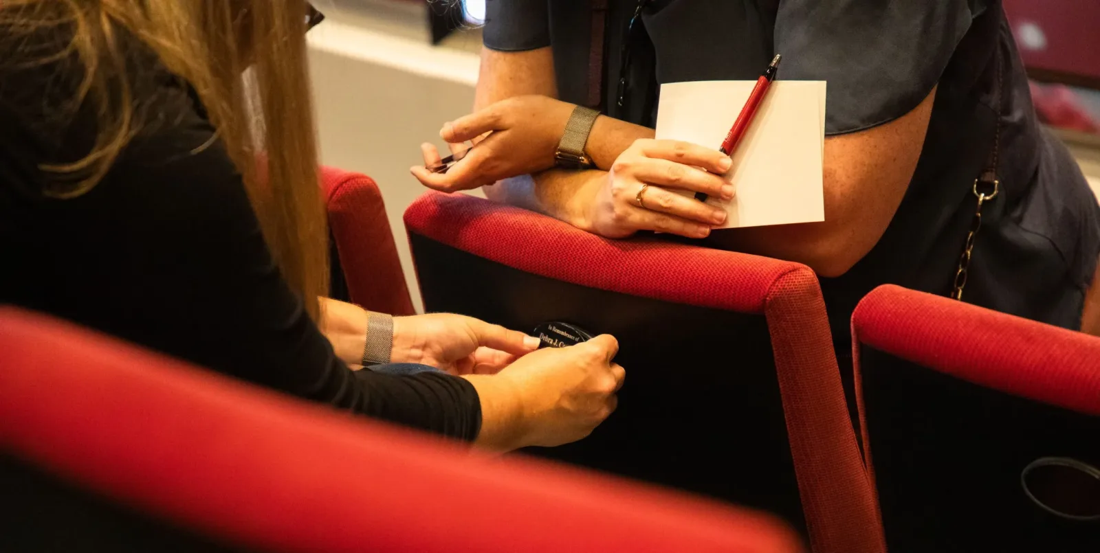A woman putting a donor name plate on the back of a seat while another woman leans over the back of the seat.