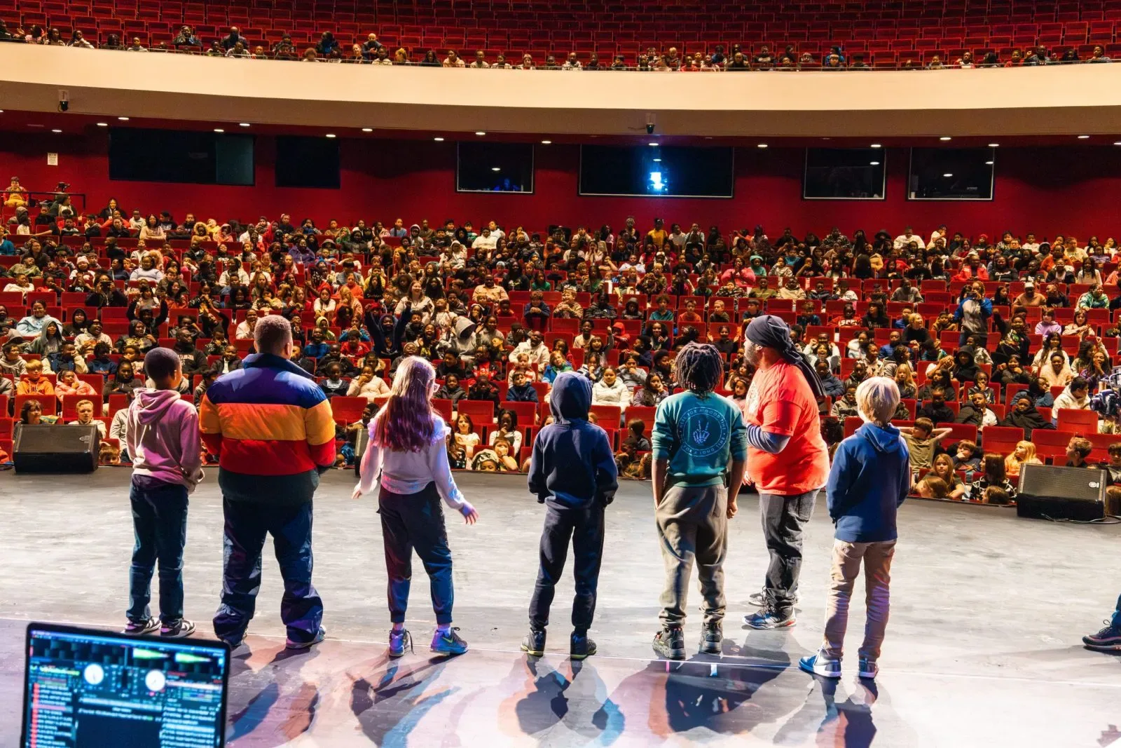 A group of children standing on stage in front of an audience of children in the Koger Center auditorium.