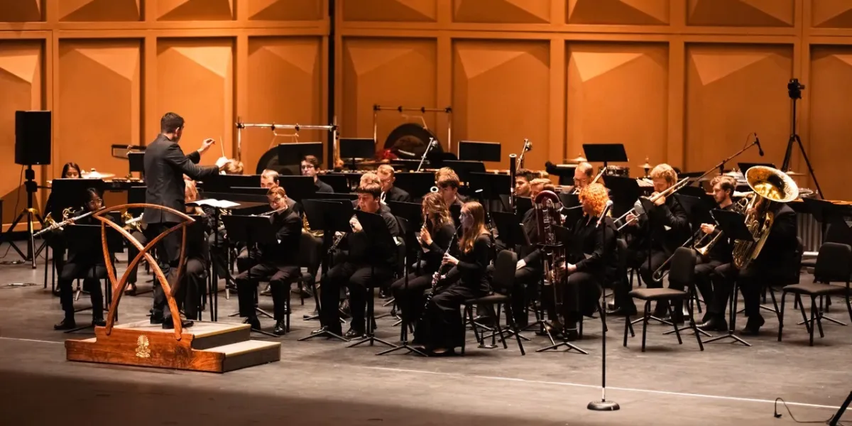 Conductor leading a seated concert band performing on the Koger Center stage.