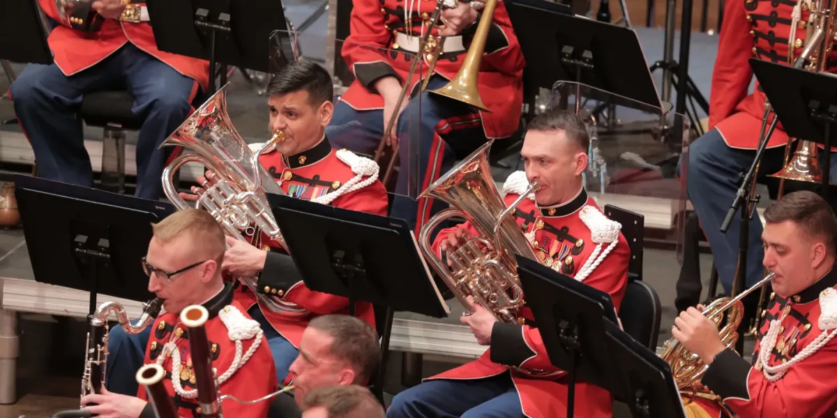 A close up photo of several bras players in the Marine band. Each musician is wearing traditional red and blue Marine garb.